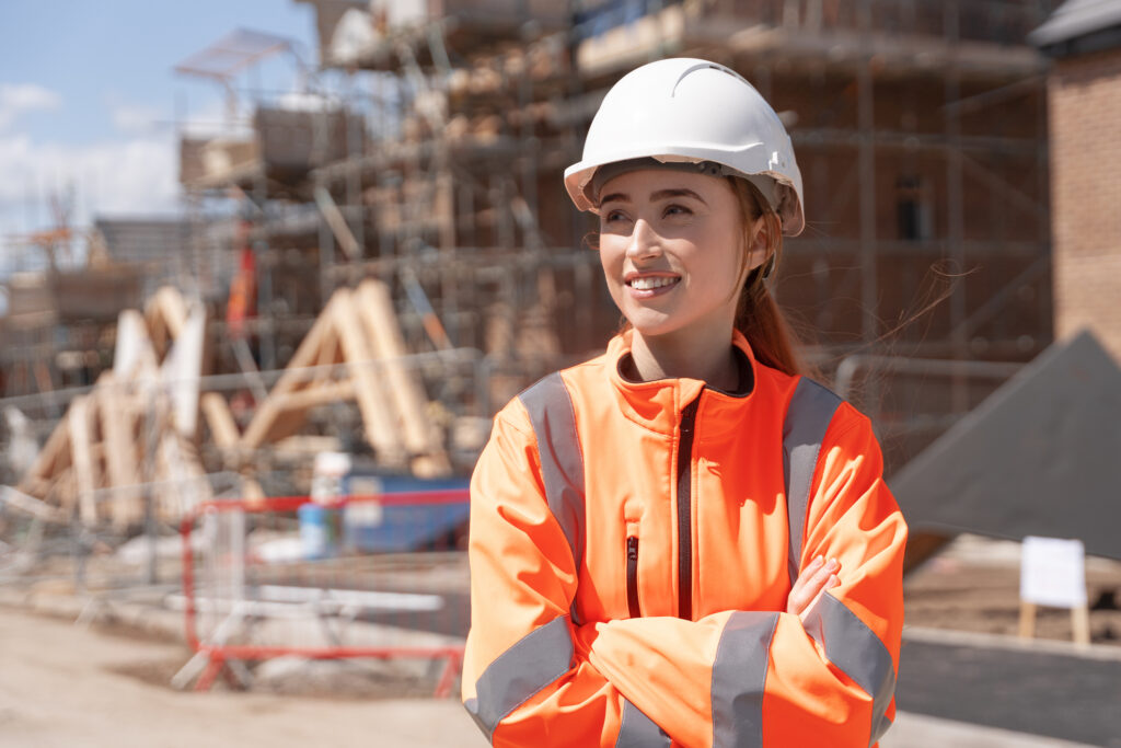 Portrait Of Young Woman Construction Worker In Safety Gear Standing Confidently On Building Site